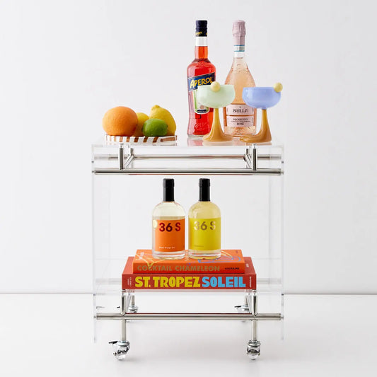 Styled photo of clear acrylic and metal bar cart styled with fruit, alcohol bottles and colourful cocktail glasses